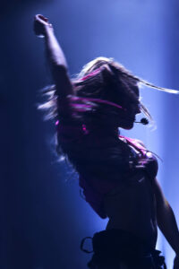 orie en plein mouvement sur scène, capturée avec un effet dynamique de lumière et de flou, lors d’un concert live. Photographie signée Yan Forhan, photographe officiel de Lorie Pester.