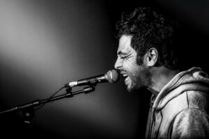 Christophe Maé en studio d’enregistrement, capturé en pleine performance vocale. Son expression intense et l’éclairage contrasté renforcent l’émotion brute de l’instant.